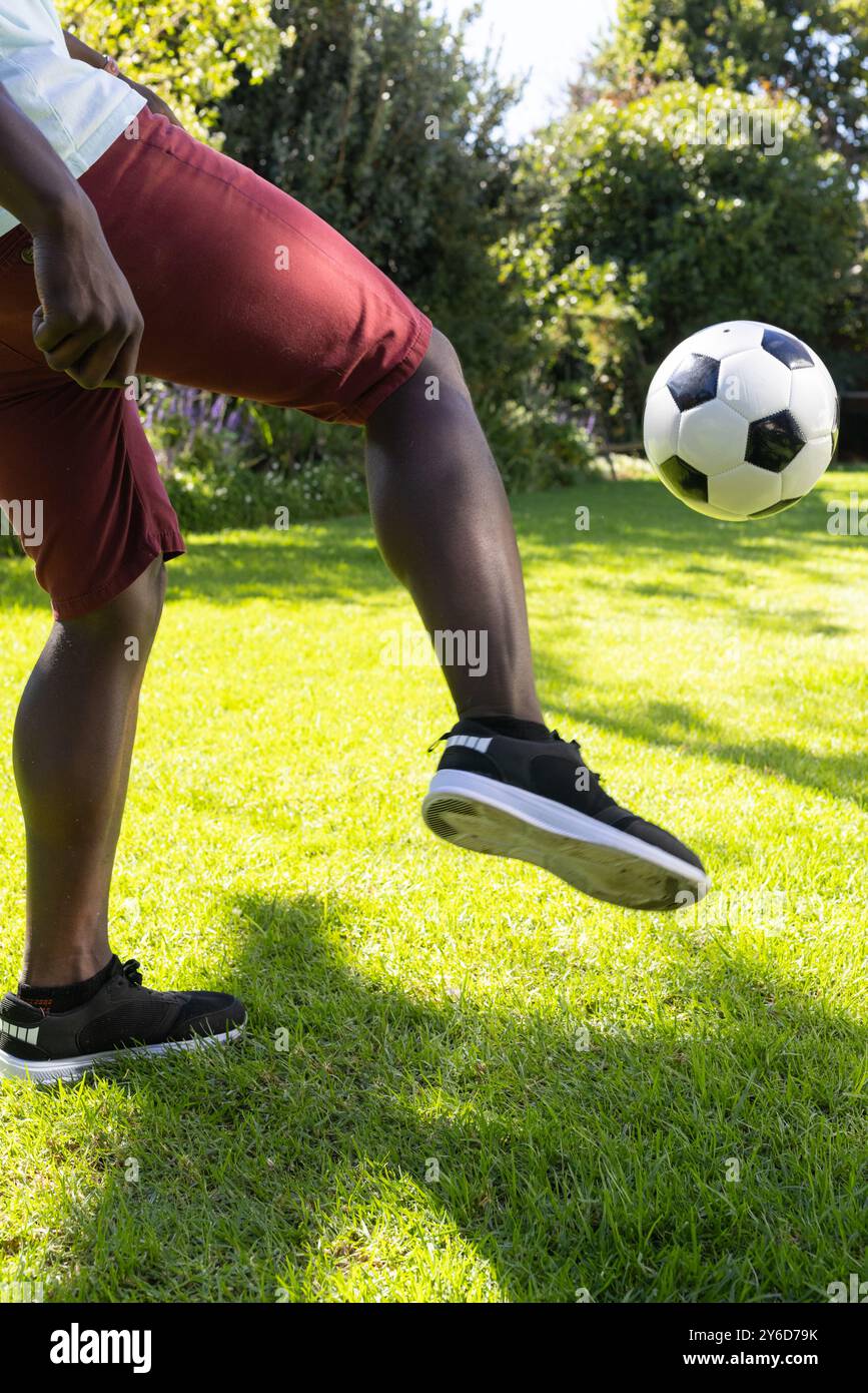 Giocando a calcio, uomo afroamericano che calcia la palla sull'erba in un parco all'aperto Foto Stock