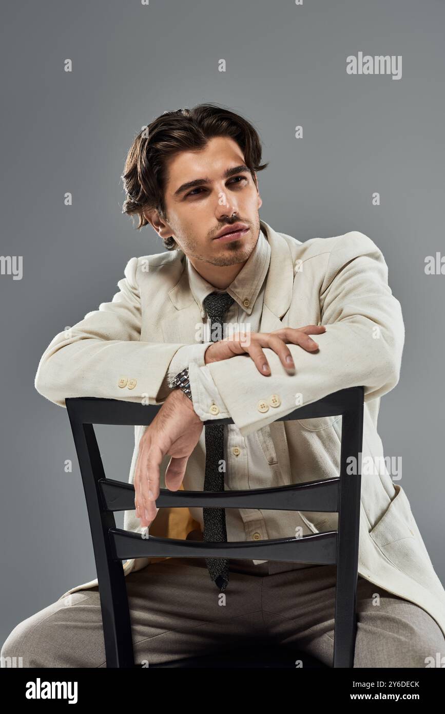 Un giovane vestito impeccabilmente con un abito formale si appoggia su una sedia, trasudando fascino ed eleganza. Foto Stock