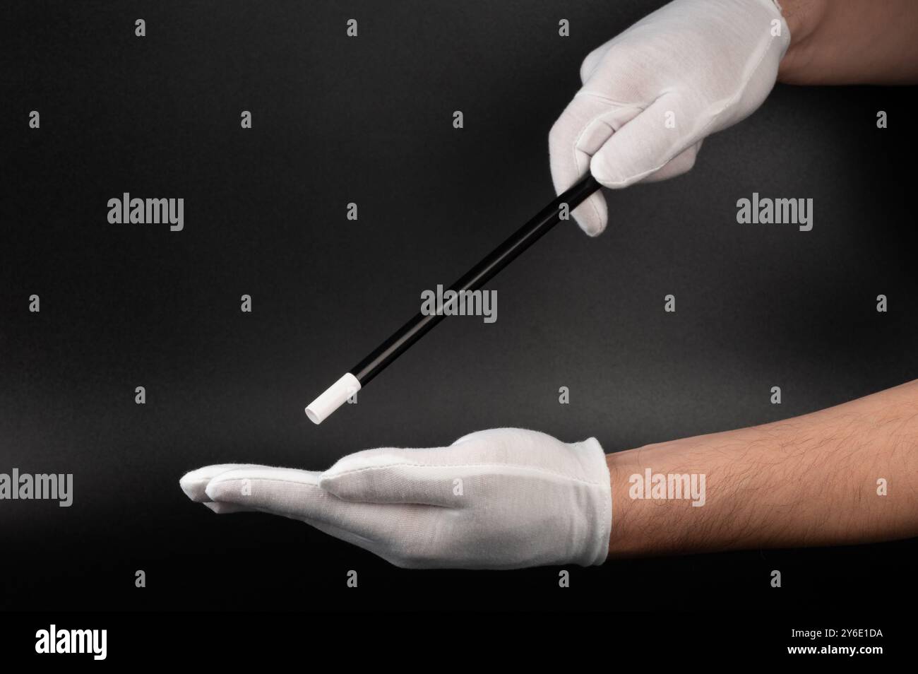 Mani in guanto bianco con bastoncino magico su sfondo nero Foto Stock