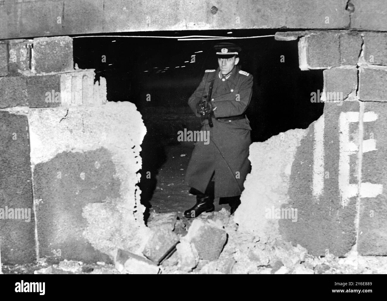 17 DICEMBRE 1962 UNA GUARDIA DI FRONTIERA DELLA GERMANIA EST CON UNA MITRAGLIATRICE PROTEGGE UN BUCO DI 9 PIEDI NEL MURO DI BERLINO A SEGUITO DI UN'ESPLOSIONE BOMBA DA OVEST SU JERUSALEMER STRASSE, BERLINO, GERMANIA OVEST. Foto Stock