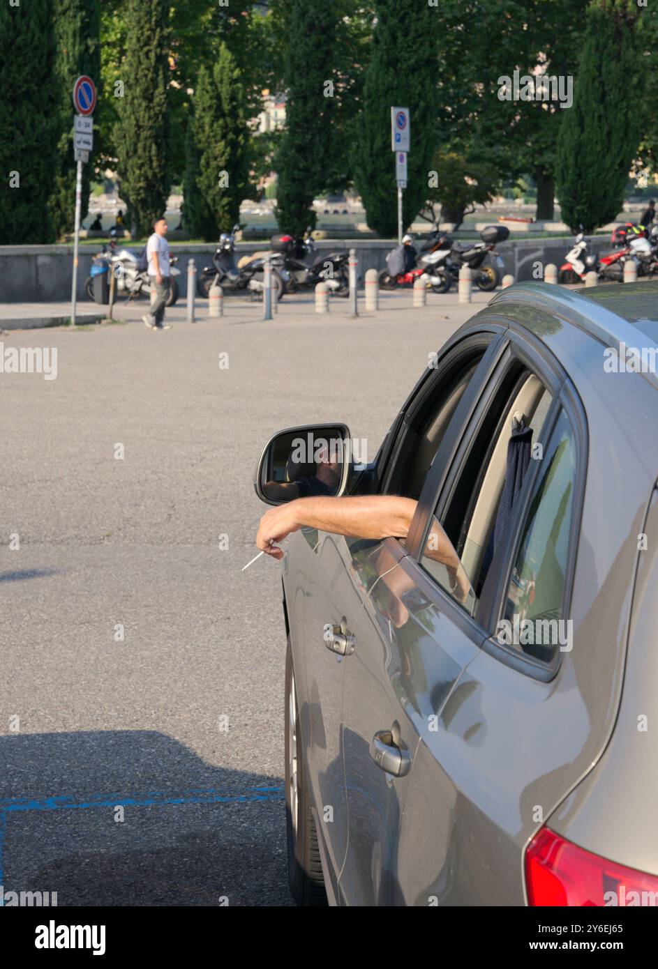 Dietro il braccio di un uomo fuori dal finestrino dell'auto con una sigaretta accesa in mano in attesa nel parcheggio Foto Stock