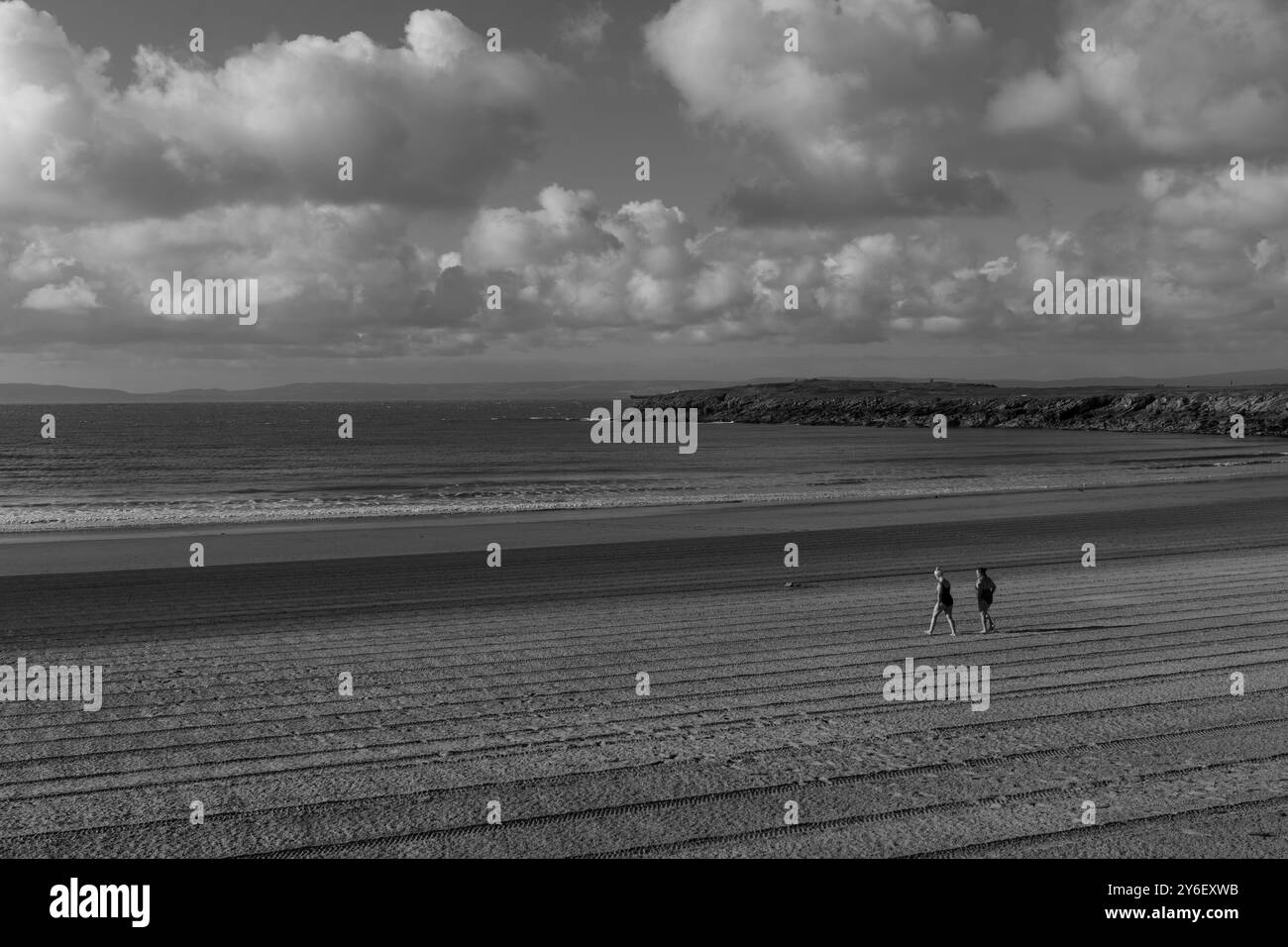 Due persone camminano su una spiaggia tranquilla e appena curata sotto un cielo pieno di nuvole. Foto Stock