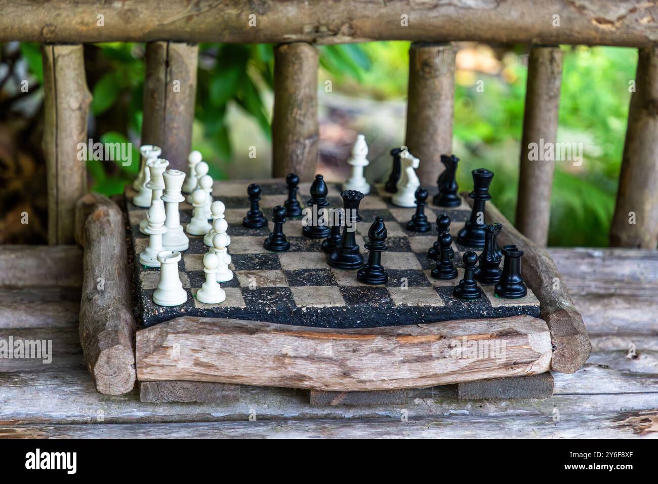 Un set di scacchi con pedine nere e bianche è posizionato a metà partita su una panca di legno rustica nei Giardini Norrviken (Norrvikens trädgårdar). Kattviksvägen, Comune di Båstad, Skåne, Svezia. Foto Stock