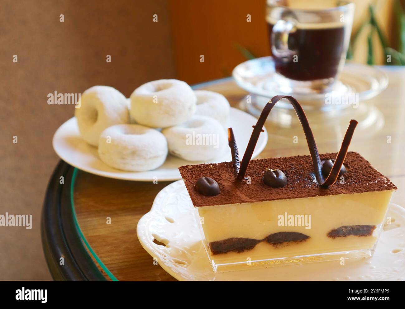Primo piano del Tiramisu italiano con ciambelle sfocate e caffè nero sullo sfondo Foto Stock