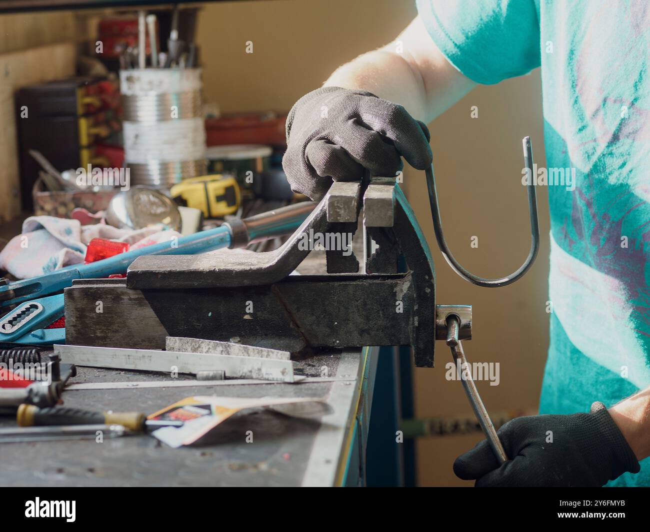 Il lavoratore di metalli piega un'asta in un'officina affollata, mostrando abilità e precisione con vari utensili. La scena cattura il lavoro manuale nella fabbricazione dei metalli Foto Stock