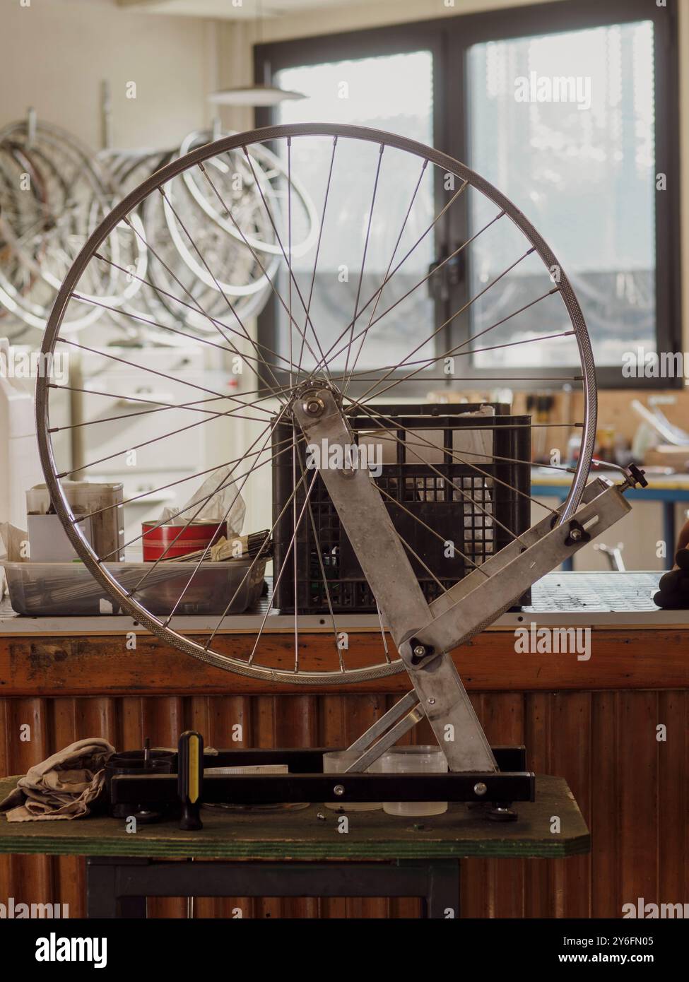 Il meccanico di biciclette centra una ruota su un cavalletto in un'officina, regolando i raggi con precisione per prestazioni ottimali. Questa immagine mette in risalto il mestiere Foto Stock