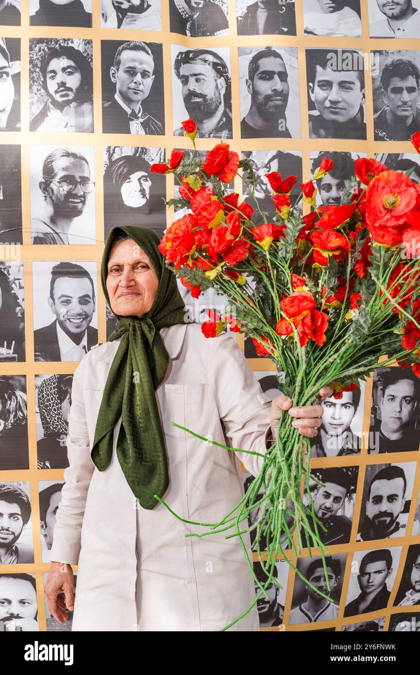 Ritratto di una donna con un mazzo di papaveri, la cui sorella studentessa è stata uccisa dal regime iraniano, di fronte ai volti dei martiri della rivolta in Iran 2022 - 2023. Dimostrazione per celebrare il secondo anniversario della rivolta in Iran, per denunciare la brutale repressione del regime iraniano e l'escalation delle esecuzioni negli ultimi mesi. Organizzato da varie organizzazioni. Francia, Parigi, 13 settembre 2024. Foto di Patricia Huchot-Boissier / Agence DyF. Foto Stock