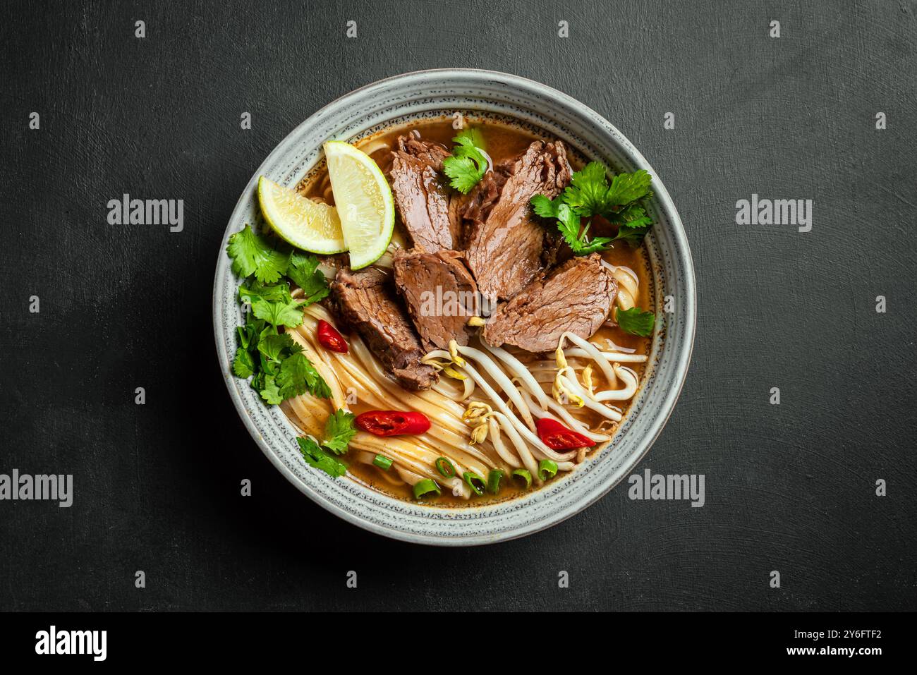 Zuppa vietnamita Pho Bo, ciotola di zuppa asiatica fresca con spaghetti di riso, carne di manzo, erbe, germogli di soia e peperoncino su sfondo nero, vista dall'alto. asi fatto in casa Foto Stock