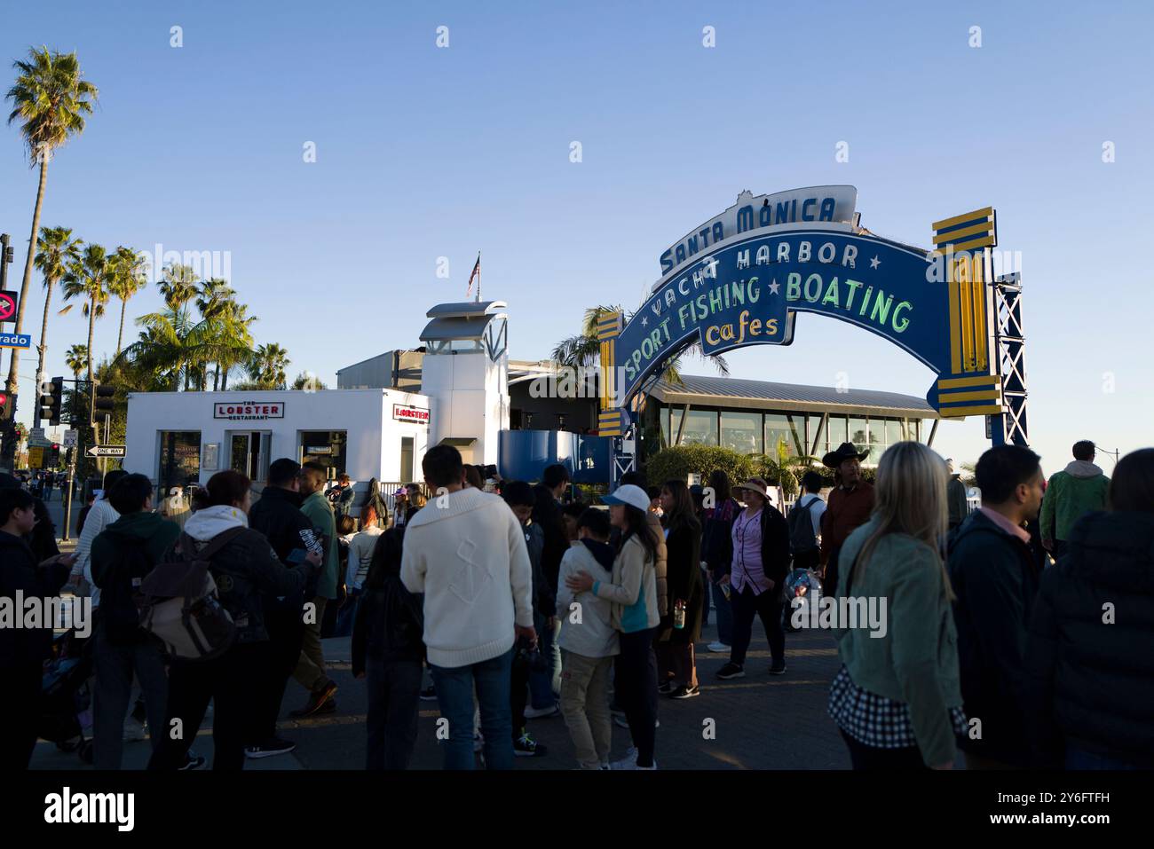 La folla si riunisce sotto il cartello del porto degli yacht di Santa Monica, godendosi una giornata di ristoranti all'aperto, pesca sportiva e nautica lungo il pittoresco lungomare. Foto Stock