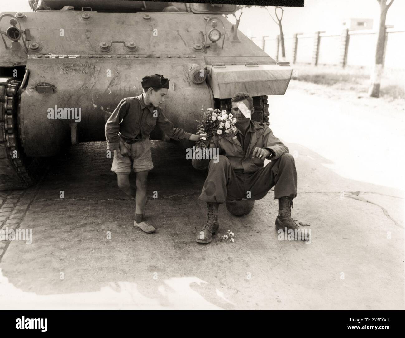 1944 , 4 giugno , ROMA , ITALIA : un bambino italiano regala fiori a un soldato americano alle porte di Roma . Gli alleati entrarono in città da sud in via CASILINA , APPIA e TUSCOLANA . Probabilmente il soldato americano ferito all'occhio destro, con la sua uniforme macchiata di olio e seduto sul casco, fu il pilota di carri armati che guidò il carro armato visto nella foto, esaurito dalla lotta alla porta di Roma contro i nazisti e i fascisti italiani . I fiori devono essere stati delle piccole rose con le spine perché il bambino li tiene in mano protetti da un pezzo di carta o da un fazzoletto. Foto sconosciuta Foto Stock