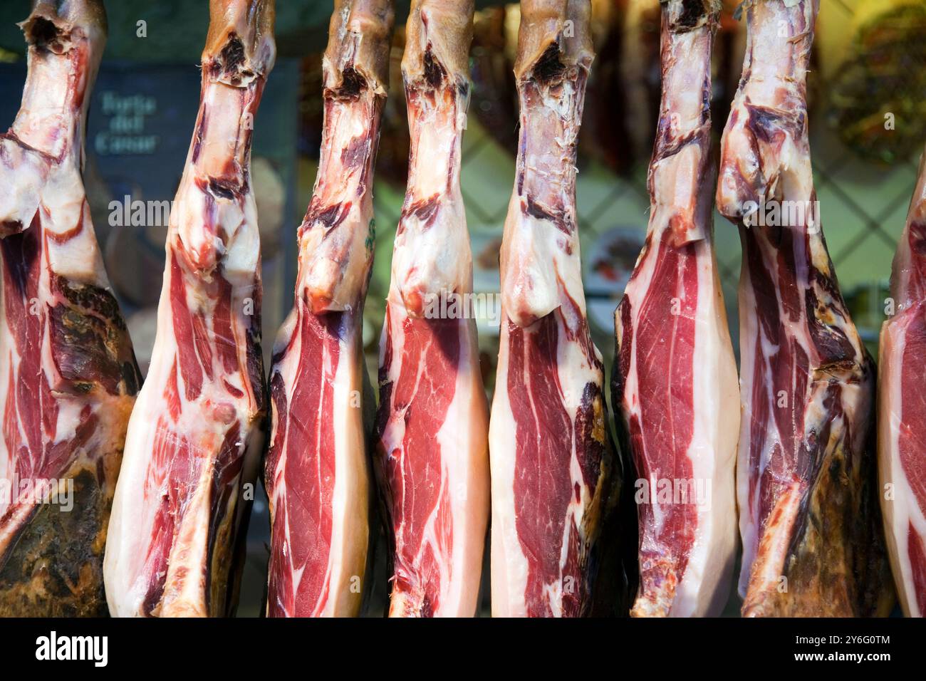 Una varietà di prosciutti stagionati è appesa in una macelleria al mercato la Boqueria, che mostra la vibrante cultura gastronomica di Barcellona. Foto Stock