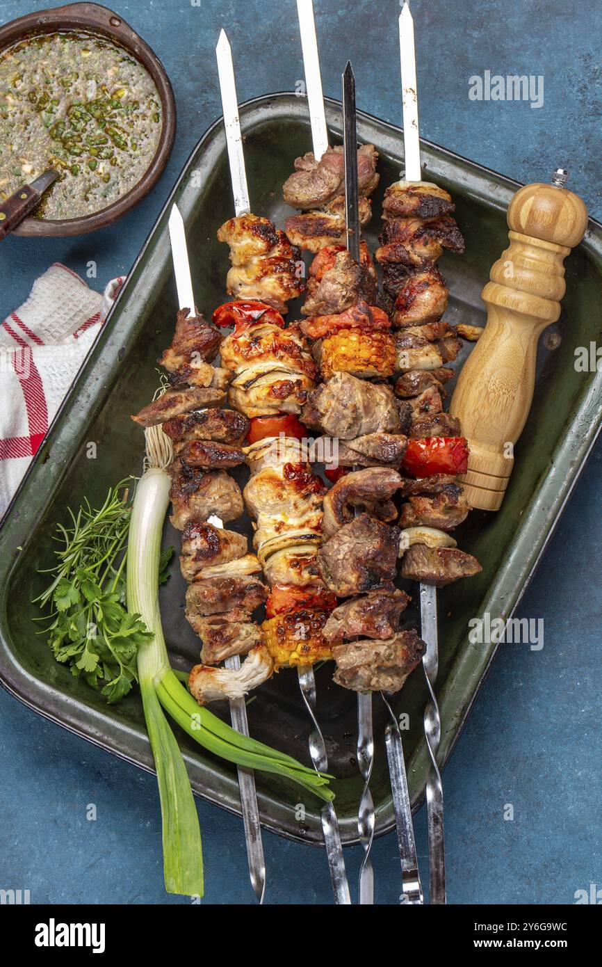 Fotografia gastronomica, barbecue di carne di maiale alla griglia, spiedini di pollo e verdure sul vassoio Vista dall'alto, disposizione piatta. Sfondo blu Foto Stock
