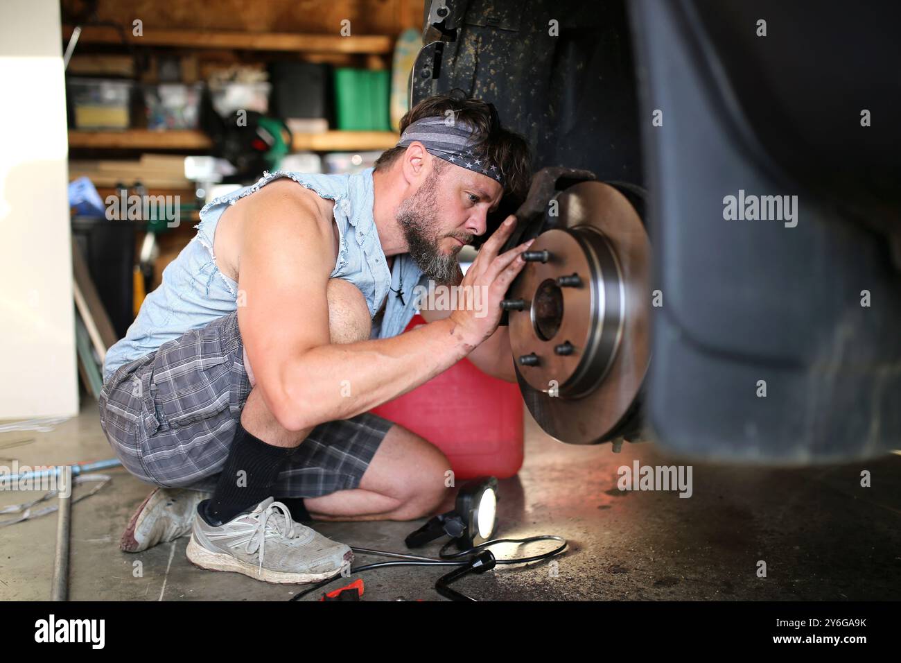 Un bel giovane barbuto sta riparando i freni dell'auto sul suo furgone nel suo garage di casa. Foto Stock