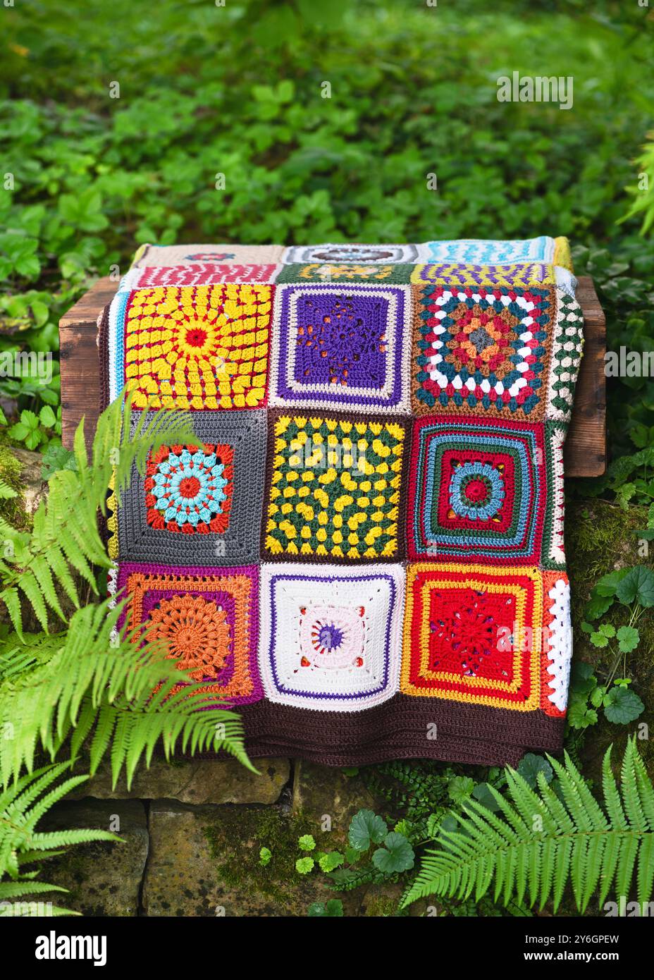 Nonna a uncinetto d'epoca fatta a mano su una scatola rustica in legno nel giardino del cottage. Lavorare a maglia nello stile del patchwork. Concetto di hobby. Copia spazio. Foto Stock