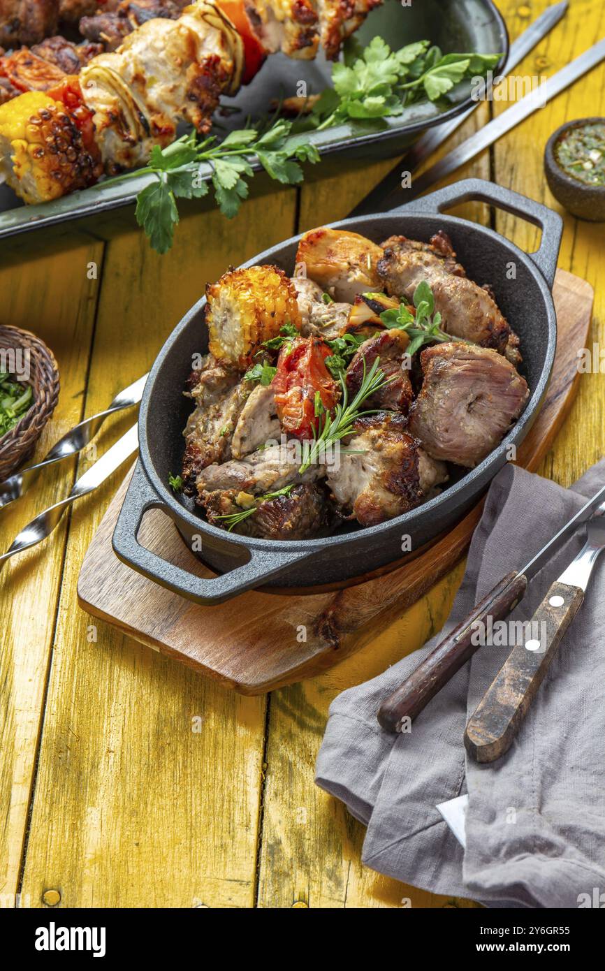 Cibo, carne grigliata alla griglia, maiale, pollo e verdure su una teglia in ghisa. Spiedini grigliati su sfondo giallo in legno. Vista dall'alto Foto Stock