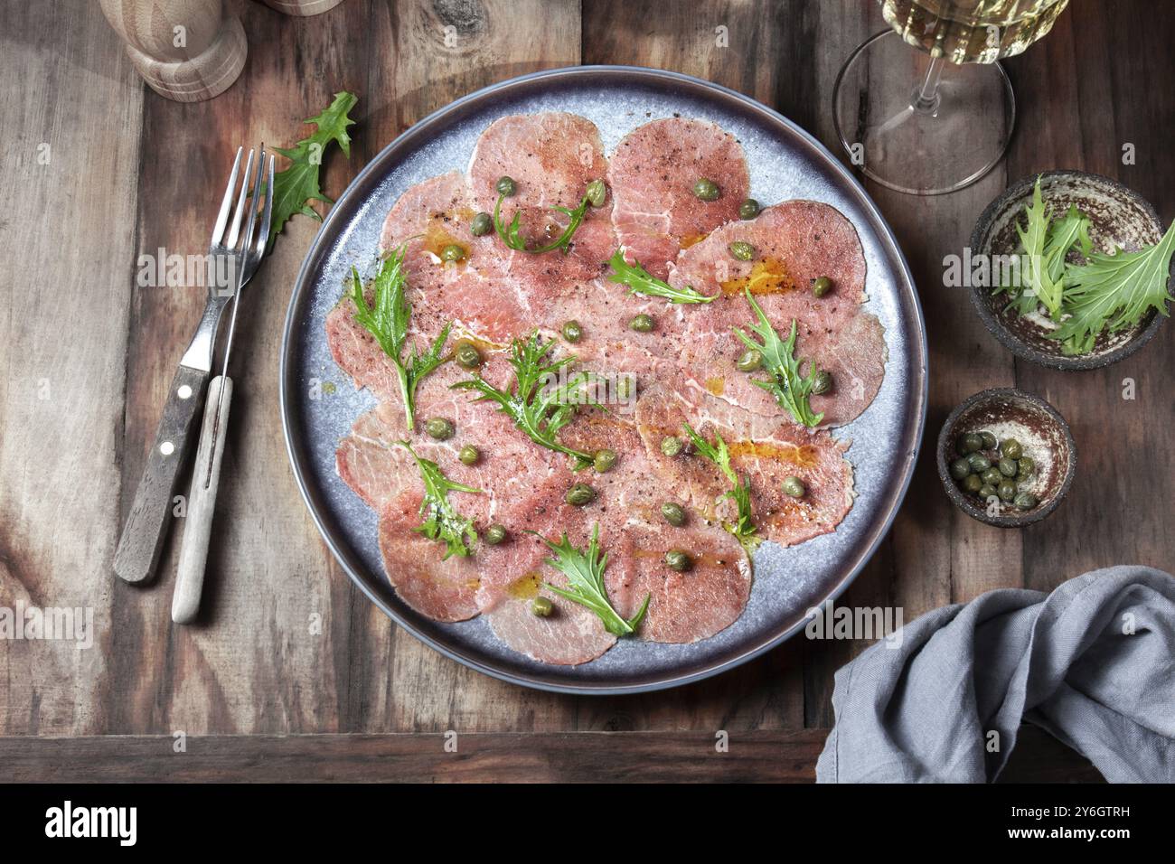 Cibo, cibo, carpaccio di manzo marmorizzato con rucola e capperi su piatto grigio con vino bianco, sfondo in legno, vista dall'alto Foto Stock