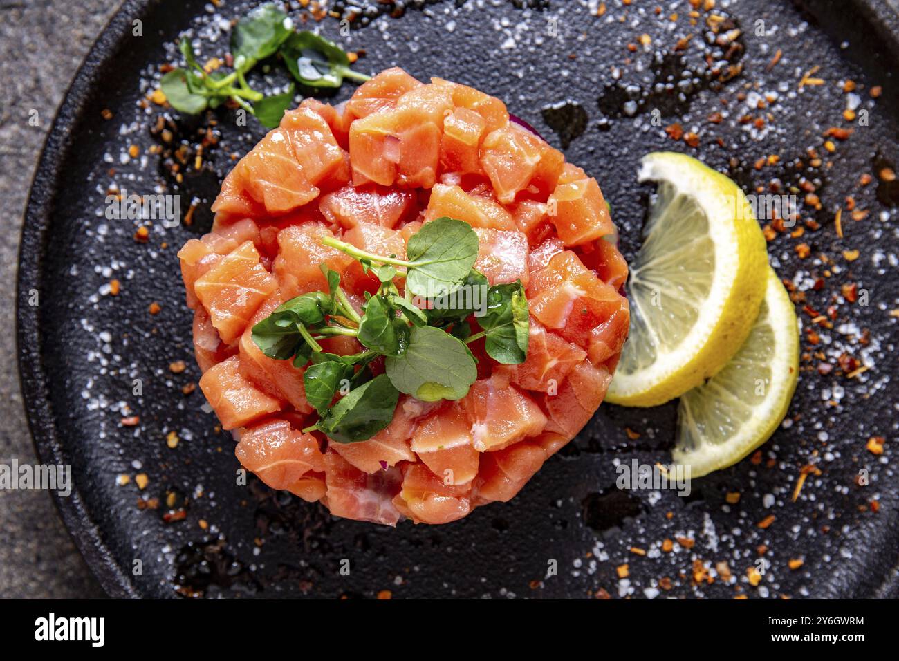 Cibo, salmone crudo, insalata di cipolle viola all'avocado servita nell'anello culinario su un piatto nero. Sfondo nero in cemento Foto Stock