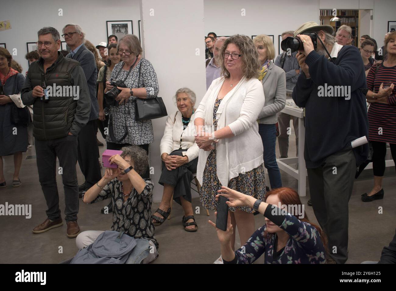 Marketa Luskacova fotografa (con le mani in ginocchio) a una festa per la sua mostra presso la MPF Martin Parr Foundation Bristol UK. Persone che ascoltano Martin Parr . 2019, 2010 anni, HOMER SYKES Foto Stock