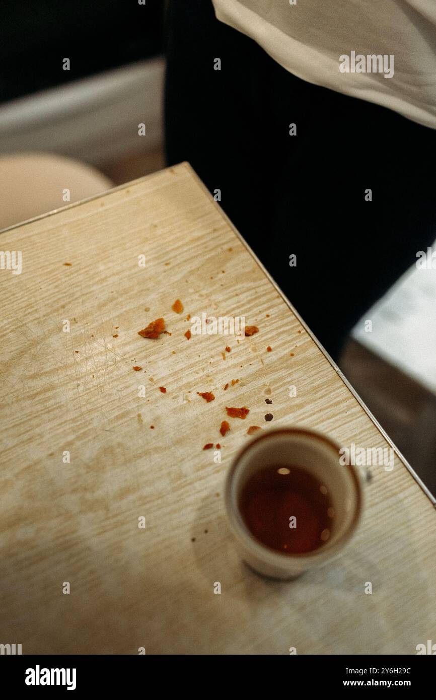 Macchie luminose di salsa rossa macchiano il piano di legno, mentre una piccola tazza si trova nelle vicinanze. Questo momento cattura i resti di un delizioso pasto condiviso con Foto Stock