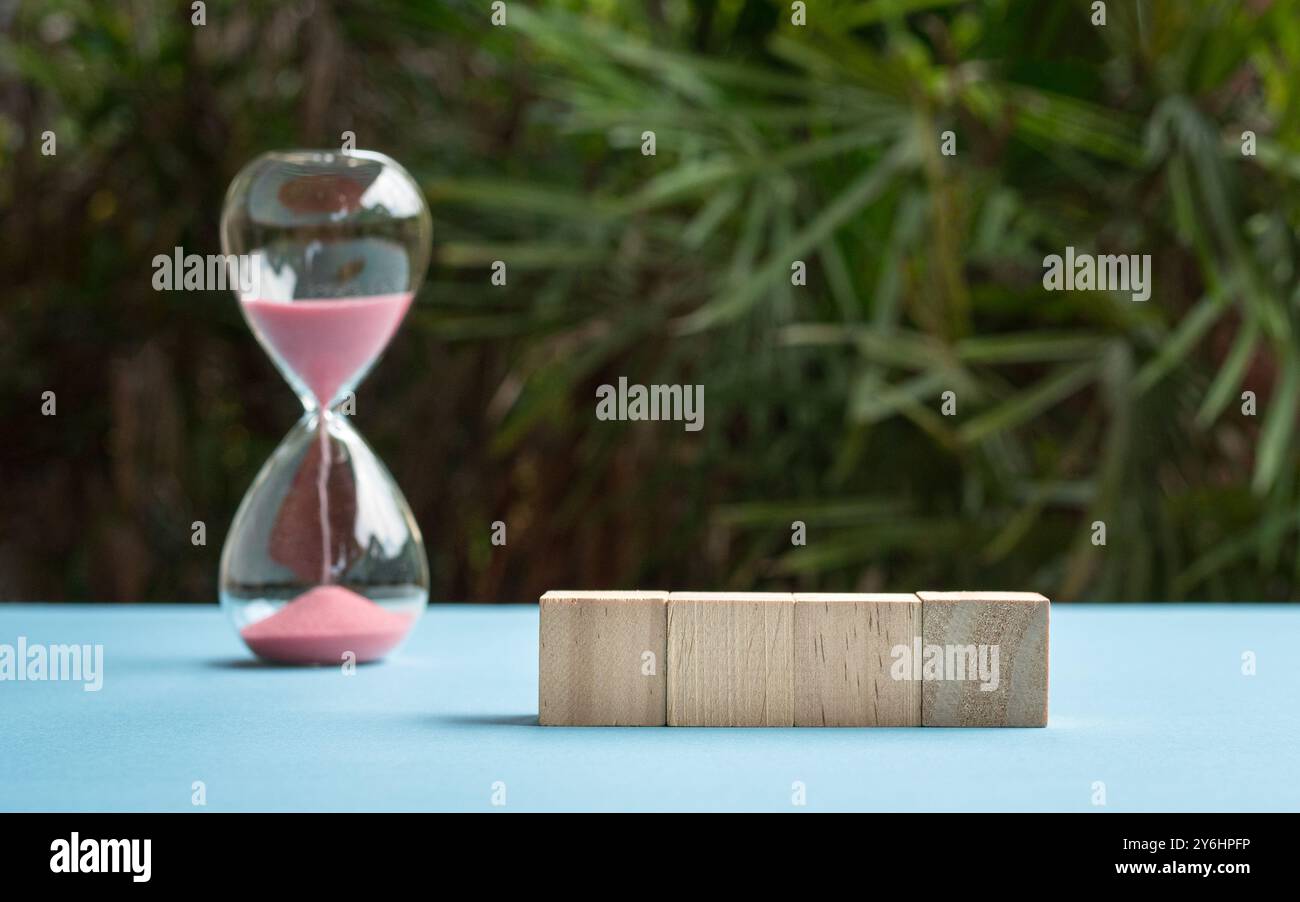 Quattro blocchi di giocattoli di legno vuoti in fila sul tavolo e accanto al timer di sabbia. Sfondo naturale. Foto Stock
