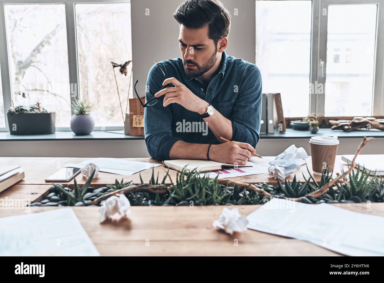 Lunga giornata lavorativa. Un giovane stanco che scrive qualcosa nell'organizzatore personale mentre si siede in ufficio Foto Stock