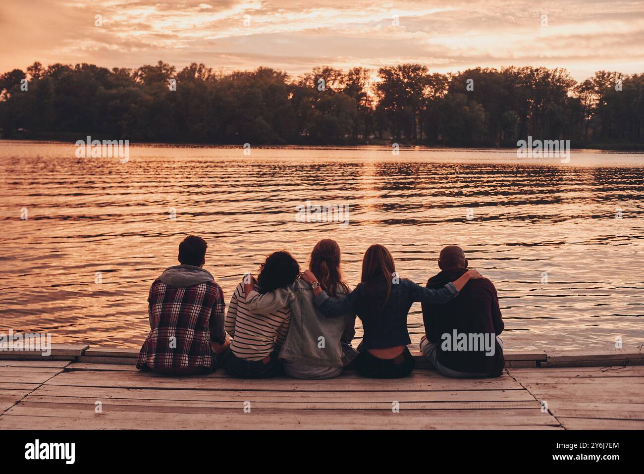 Tra i migliori amici. Vista posteriore dei giovani in abbigliamento casual che si abbracciano mentre sono seduti sul molo Foto Stock