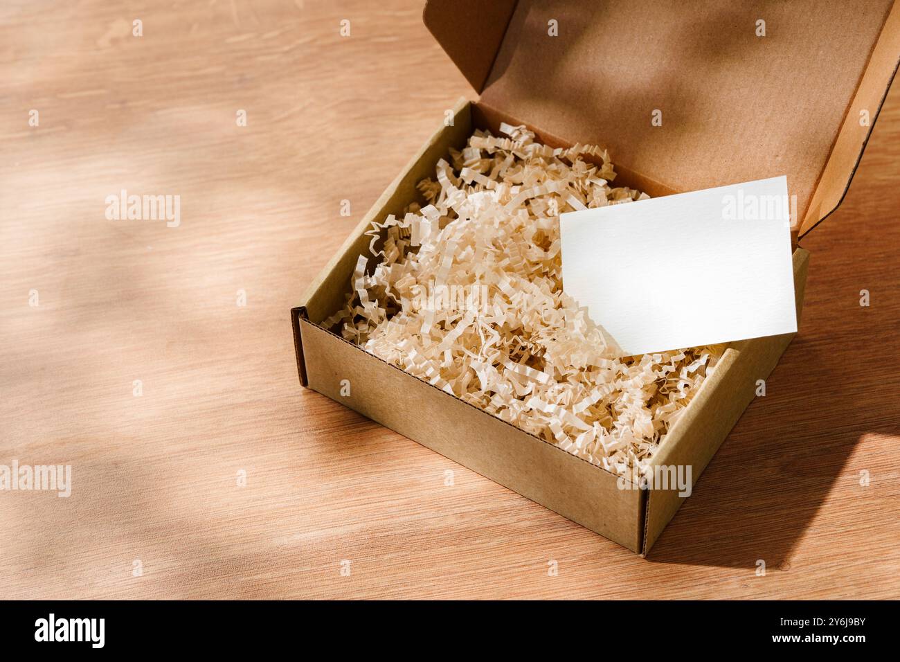 Scatola di cartone aperta riempita di carta triturata e un cartoncino vuoto su una superficie di legno Foto Stock