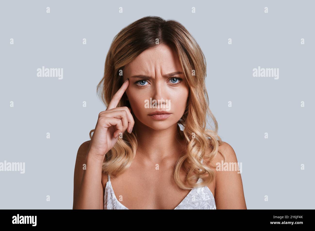 Emozione negativa. Giovane donna frustrata che guarda lontano e gesta mentre si trova in piedi su sfondo grigio Foto Stock