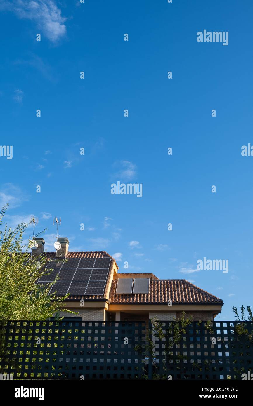 vista attraverso la recinzione esterna di una singola casa con camini e pannelli solari fotovoltaici per un'energia alternativa e sostenibile sul tetto. Foto Stock