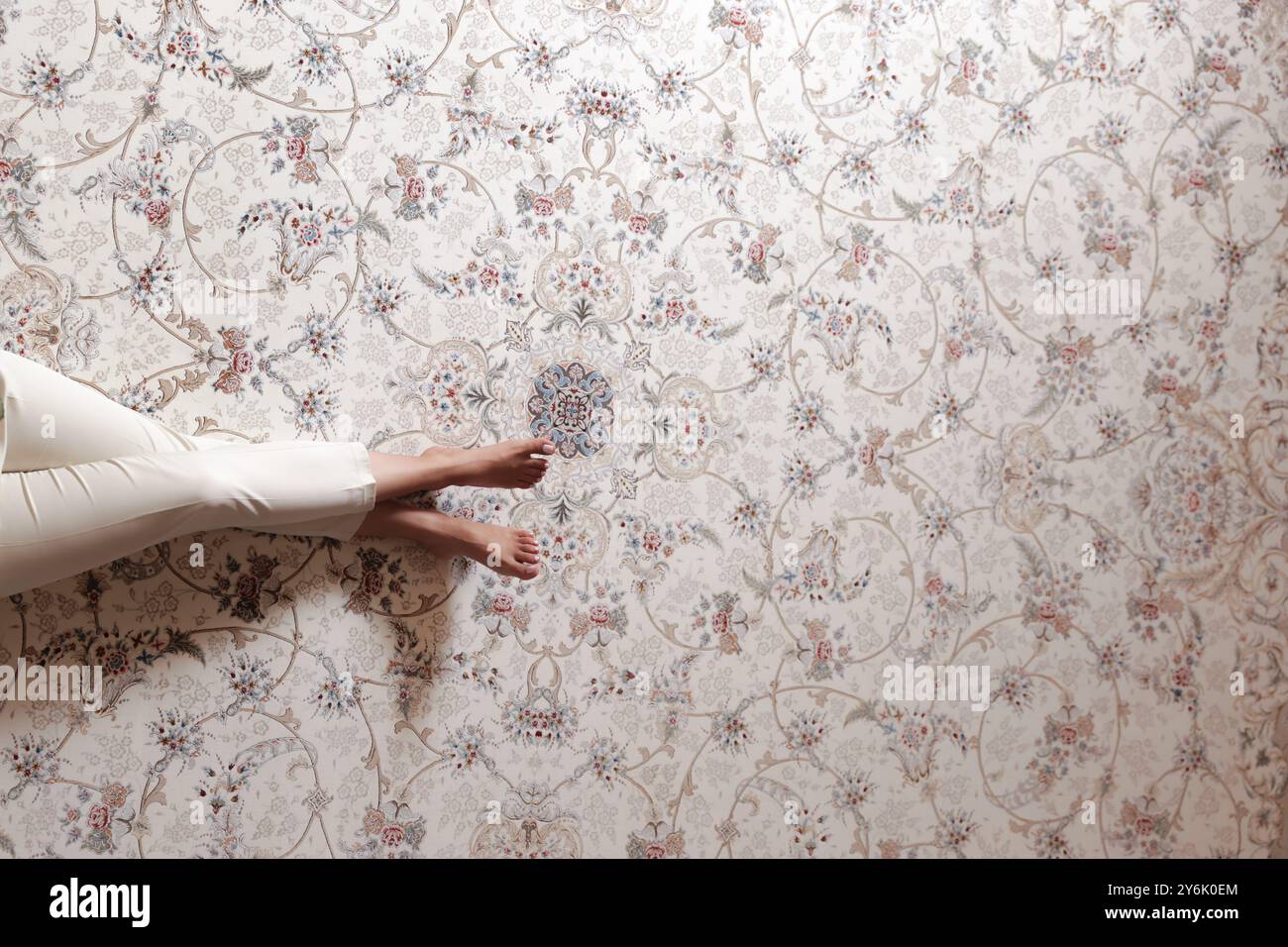 Primo piano di un bellissimo tappeto persiano con motivi floreali, che mostra un momento di relax con le gambe di una persona in vista Foto Stock