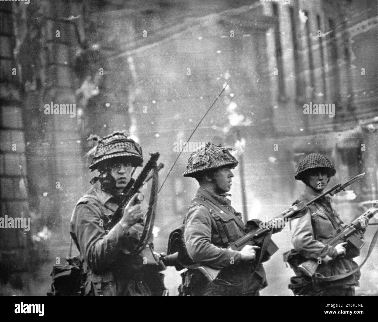 Belfast . Irlanda del Nord . Con un edificio sparato dai rivoltosi che bruciano sullo sfondo le truppe britanniche stanno di guardia nella zona di Catholic Falls Road di questa città lacerata dalla rivolta. Le truppe britanniche marciarono in città dopo una notte di violenza in cui quattro persone erano morte. 15 agosto 1969 Foto Stock