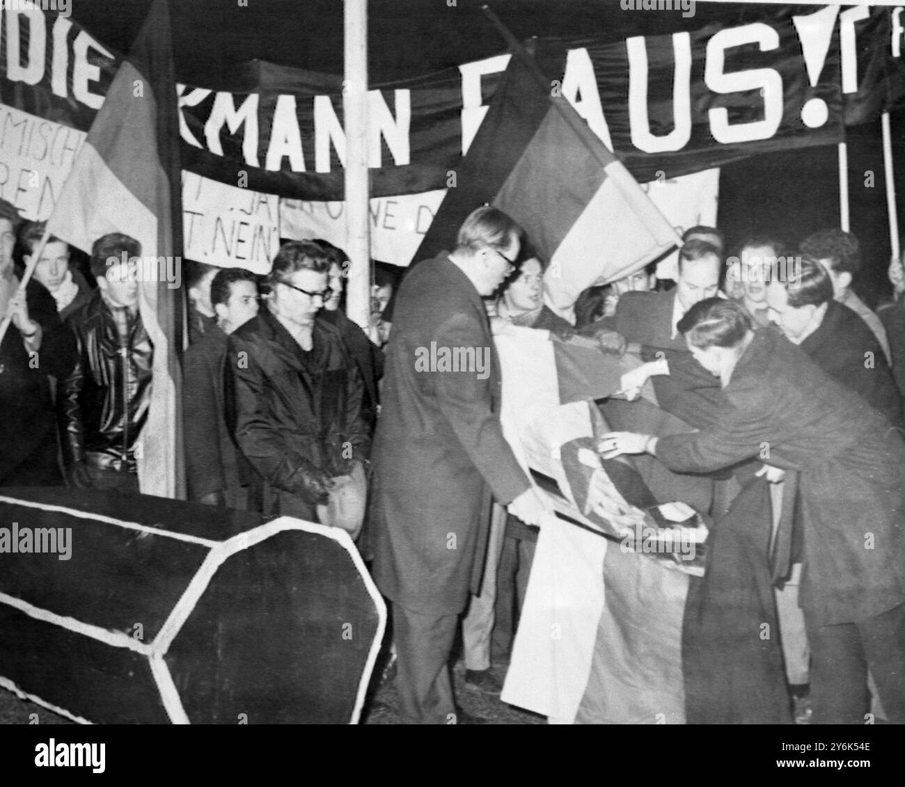 Marburgo , Germania Ovest gli studenti manifestanti arrabbiati tagliarono un emblema di zona sovietica da una bandiera tedesca durante una protesta contro un discorso per Herr Johannes Dieckmann , Presidente del Parlamento della Germania Est. Sullo sfondo c'è un cartello che dice "Dieckmann Raus" (Dioeckmann esci) e sulla sinistra c'è un modello di bara. Diverse migliaia di persone hanno sfilato per le strade qui in segno di protesta contro il discorso, ritenuto il primo mai pronunciato da un alto funzionario germanico-comunista della Germania Ovest. 14 gennaio 1961 Foto Stock