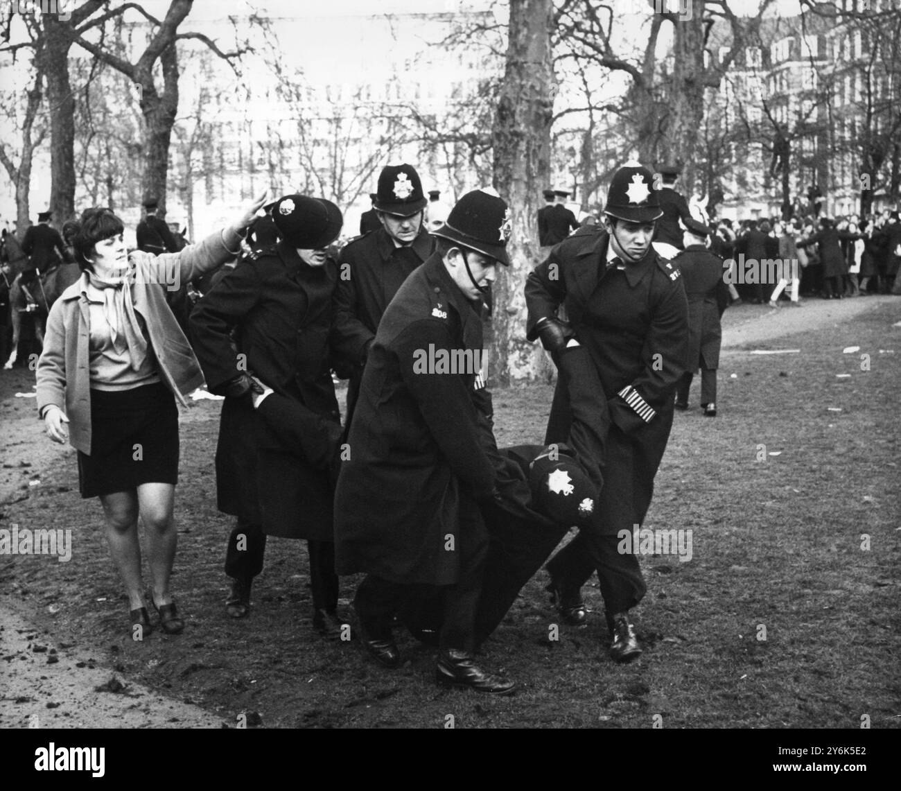 Mentre quattro poliziotti portano via un collega ferito nella battaglia del Vietnam in Grosvenor Square fuori dall'ambasciata degli Stati Uniti, una ragazza dimostrante sembra aver abbattuto l'elmetto di uno di loro. I manifestanti che protestavano contro la guerra del Vietnam combatterono con la polizia e molti furono arrestati. 17 marzo 1968 Foto Stock