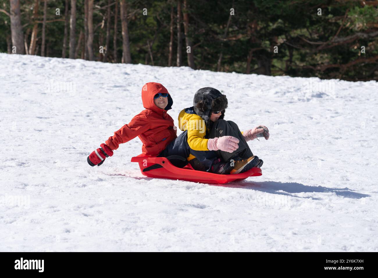 Due bambini che cavalcano insieme su una slitta sulla neve divertendosi Foto Stock