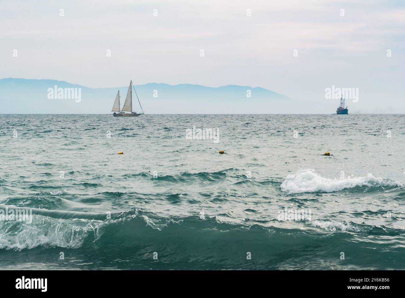 Le barche a vela navigano in acque tranquille prima di montagne nebbiose. Serenità marittima Foto Stock