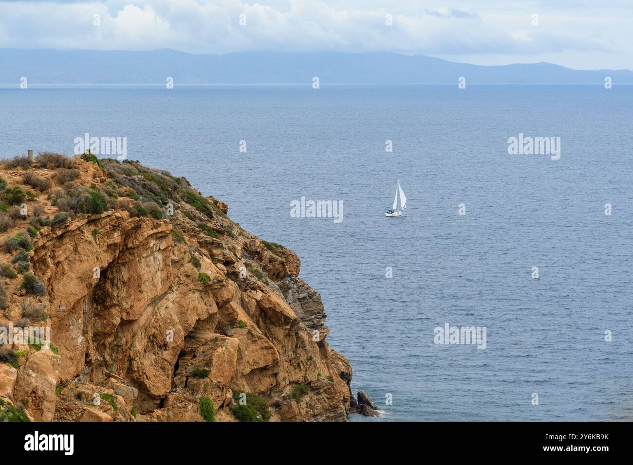 La barca a vela naviga oltre le scogliere rocciose sotto Moody Skies. Servizi sul mare Foto Stock