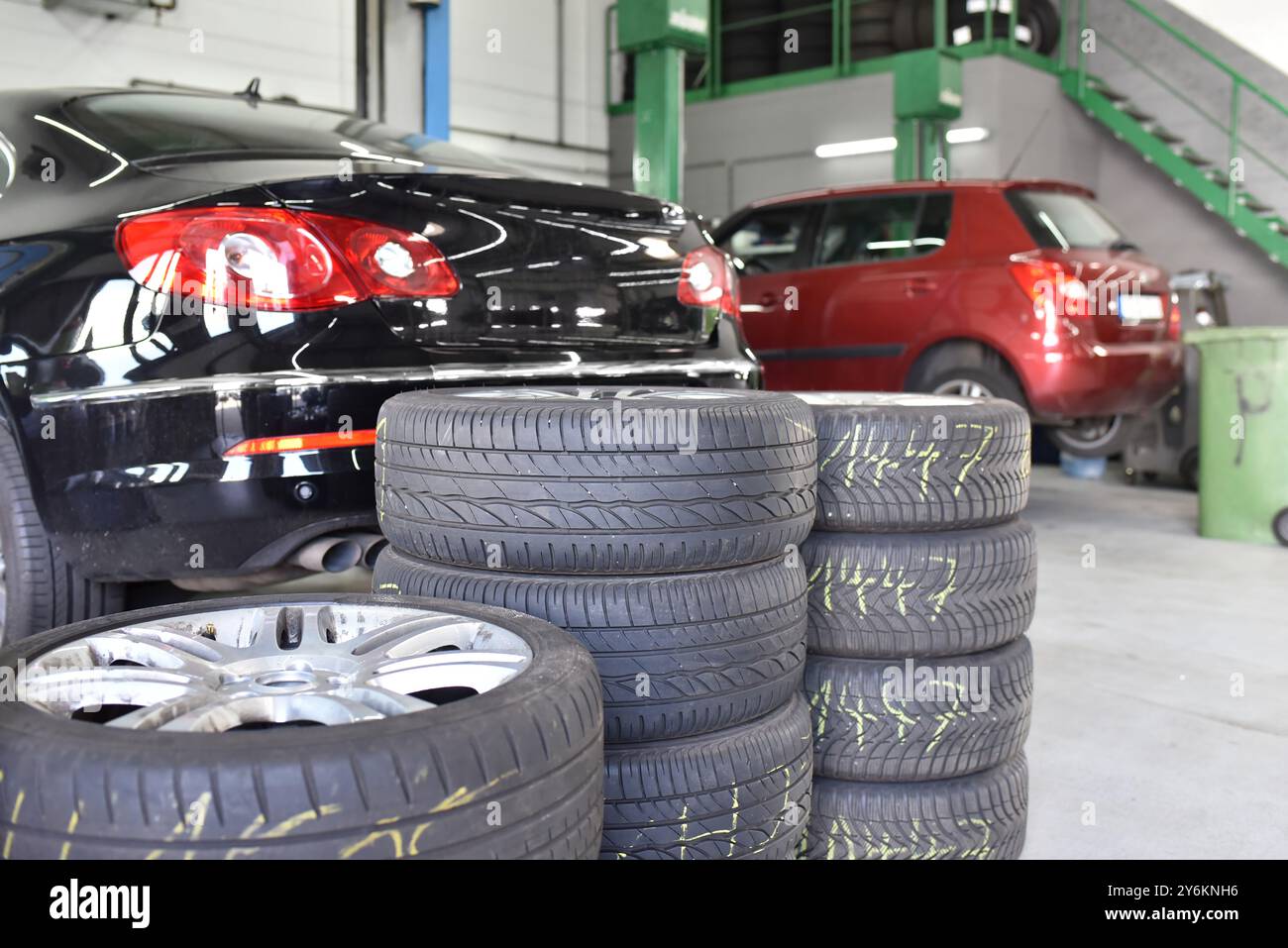 sostituzione degli pneumatici in garage - impilamento degli pneumatici in primo piano e sui veicoli in background sulla piattaforma di sollevamento Foto Stock