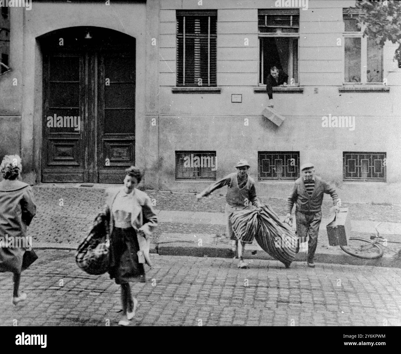 Berlino: Flashback del 20 agosto 1961 la foto mostra la fuga di un'intera famiglia appena una settimana dopo la costruzione del muro di Berlino. In fondo un uomo lascia cadere un pacco da una finestra di una casa a Bernauer Strass che ora segna il confine. Il marciapiede è Berlino ovest. Gli appartamenti nelle case furono evacuati dai comunisti il 13 agosto, ma durante i primi giorni del muro Bernauer Strasse era la via di fuga più facile, fino a quando la Germania Est sigillò tutte le porte e le finestre con i mattoni. 12 luglio 1969 Foto Stock