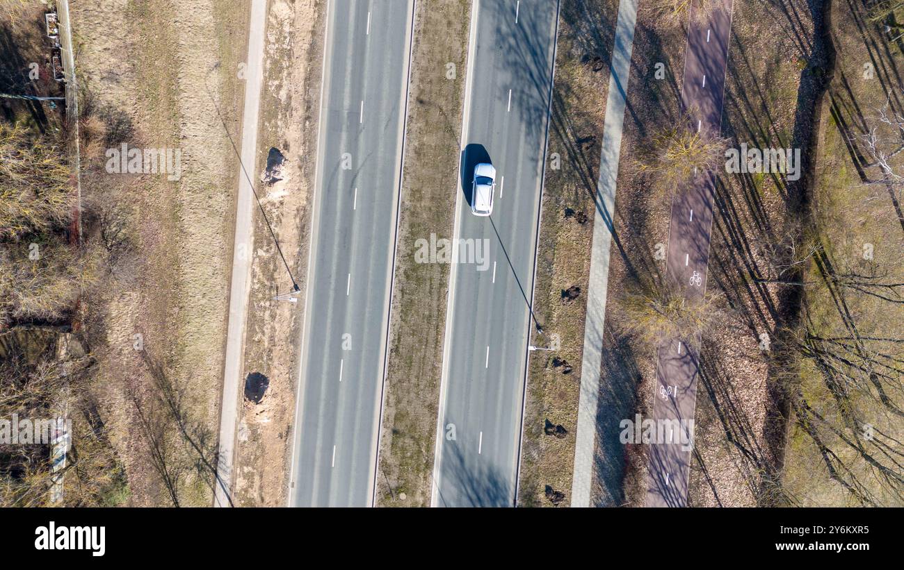 Vista aerea di un'auto che guida su una strada divisa con una mediana erbosa, circondata da alberi e sentieri Foto Stock