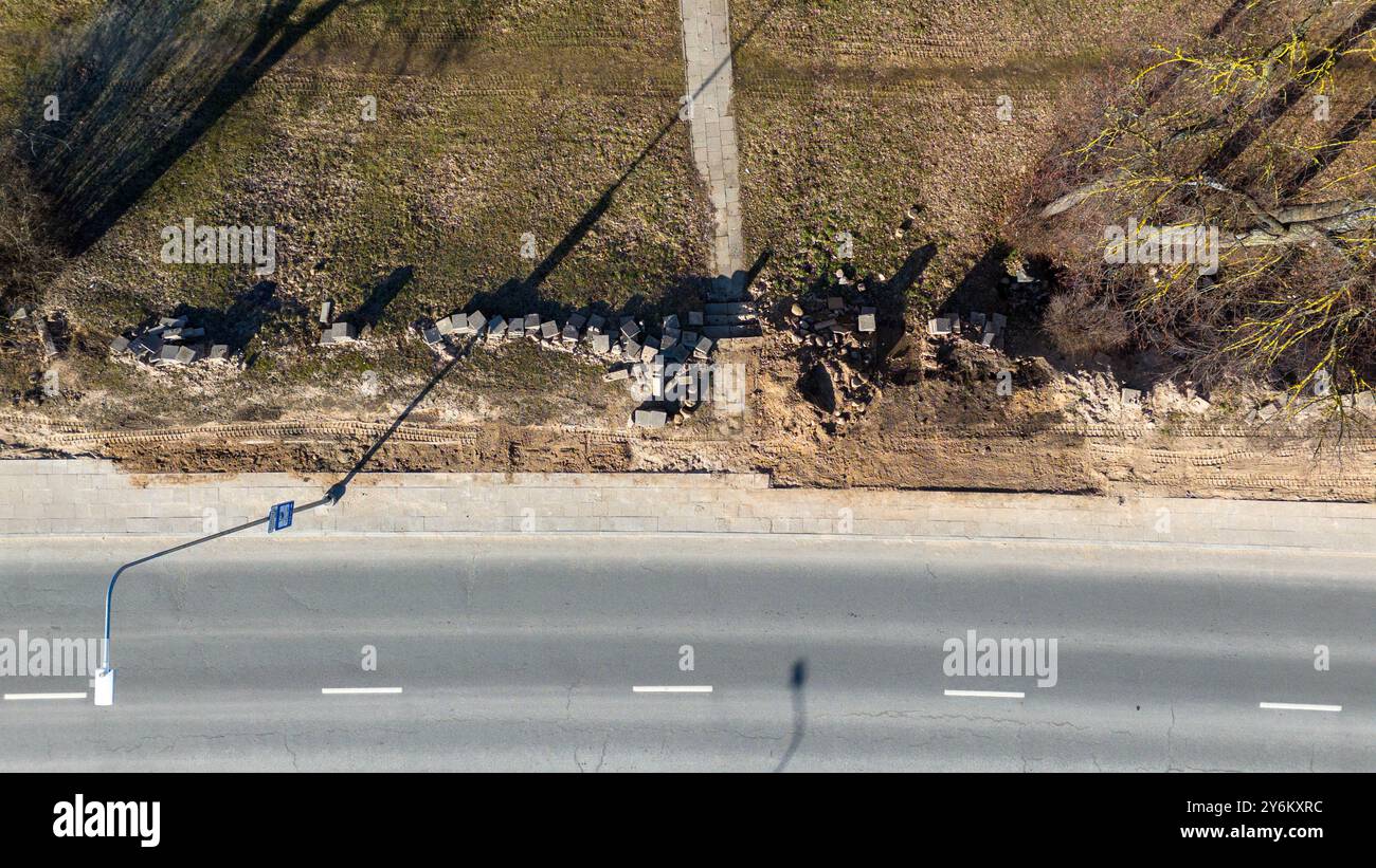 Vista aerea di un'area a lato della strada che mostra un marciapiede danneggiato con mattoni sparsi e sporcizia. L'erba è visibile lungo il marciapiede e ombreggiato Foto Stock