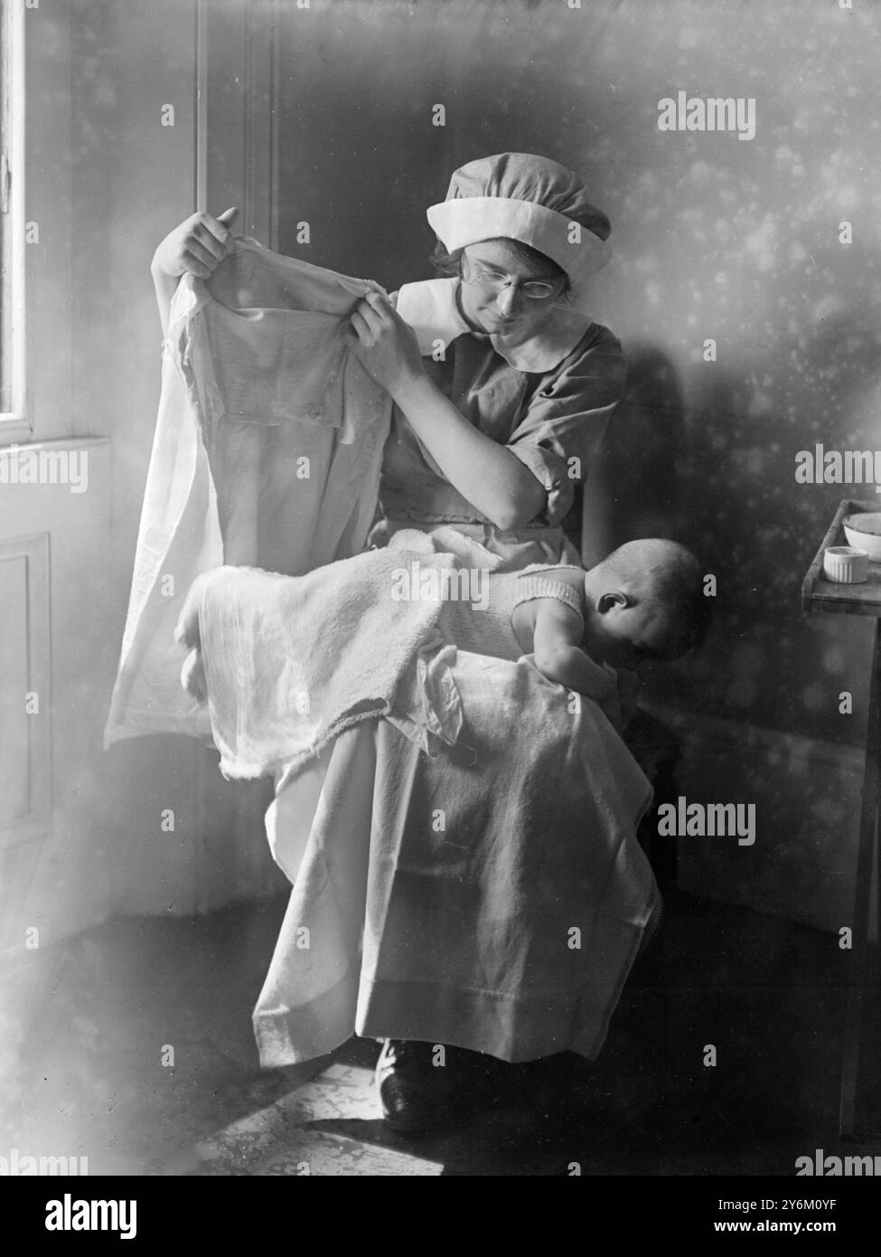 Ordine del bagno. Bambino vestito. Quando il bambino è asciutto, l'infermiera tira la cintura a maglia sulle gambe, posa due pannolini in posizione e scivola su gilet, flanella e accappatoio tutti insieme (le maniche sono state messe l'una nell'altra prima). Poi il bambino viene girato, i suoi pannolini attaccati e i suoi vestiti allacciati. Leach's Baby Book probabilmente anni '1910 anni '1920 Foto Stock