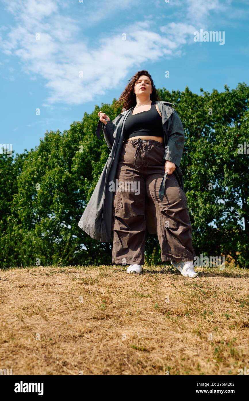 Una donna elegante e di grandi dimensioni si posa con sicurezza in mezzo a una vegetazione lussureggiante, abbracciando la sua bellezza unica. Foto Stock