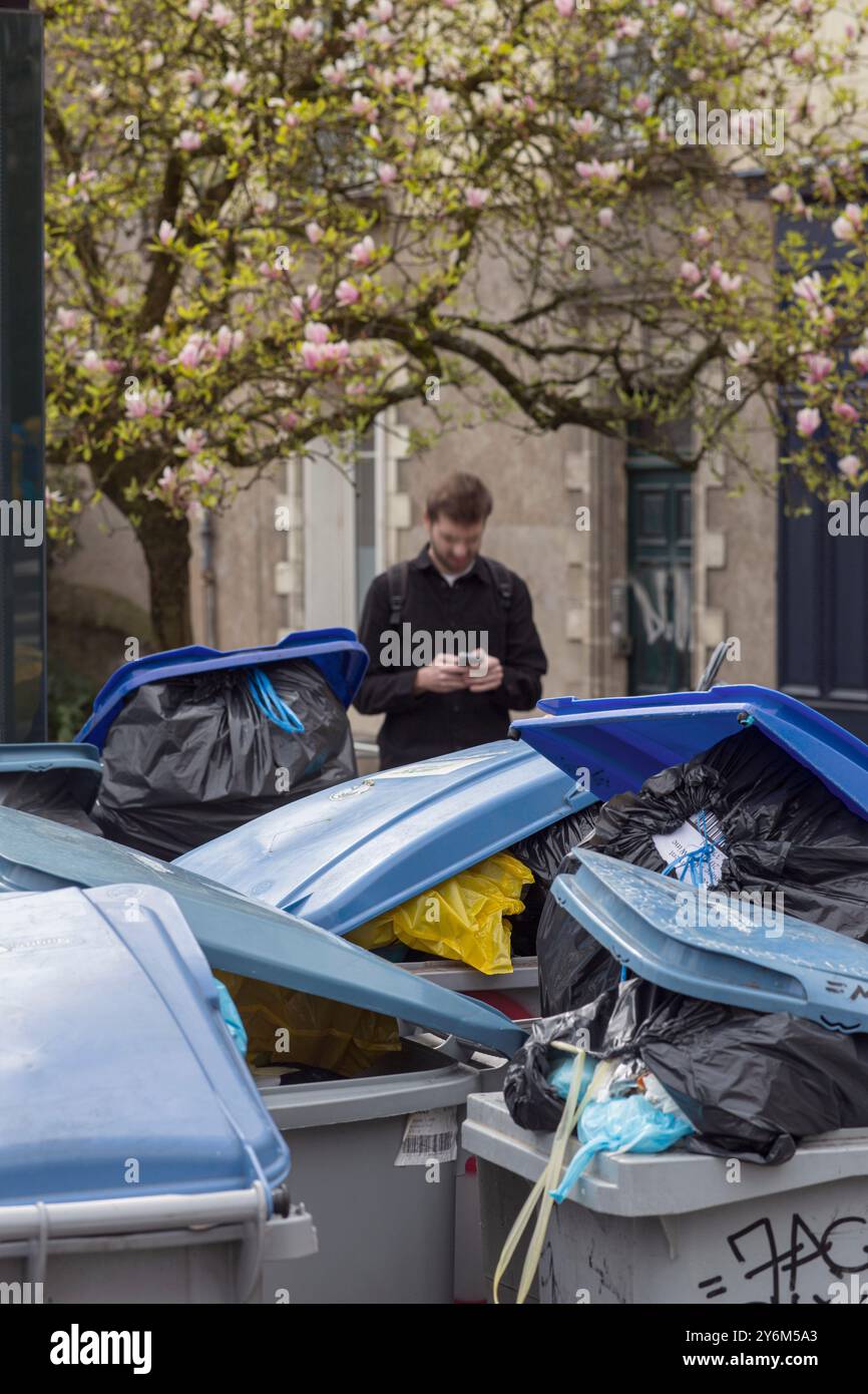 Francia, Nantes, 44, uomo che consulta il suo smartphone su un marciapiede, dove i contenitori dei rifiuti vengono accumulati durante lo sciopero dei raccoglitori di rifiuti, marzo 28, Foto Stock