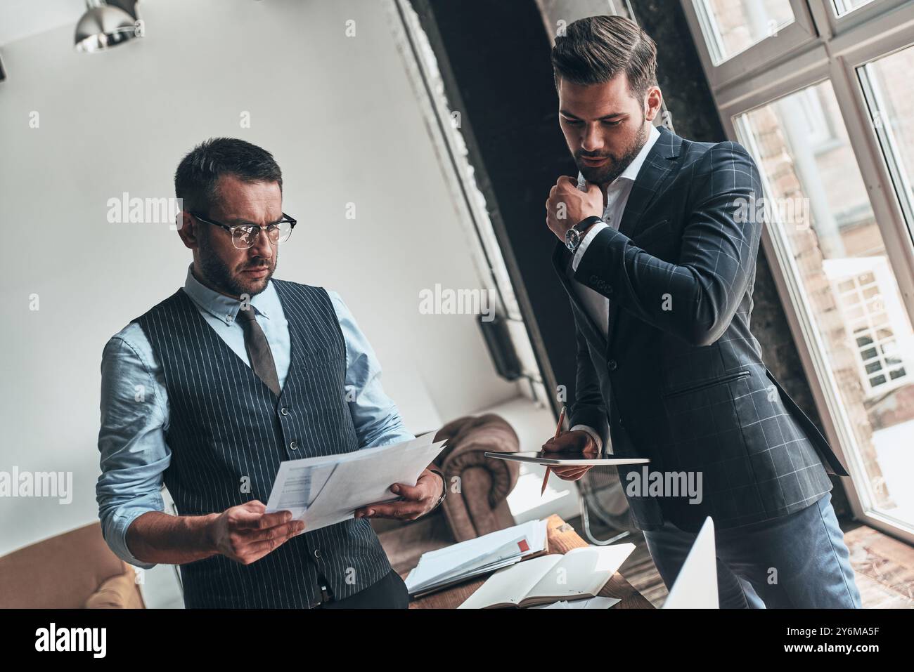 Analisi delle vendite. Due giovani uomini moderni in abbigliamento formale che lavorano insieme mentre sono seduti in casa Foto Stock