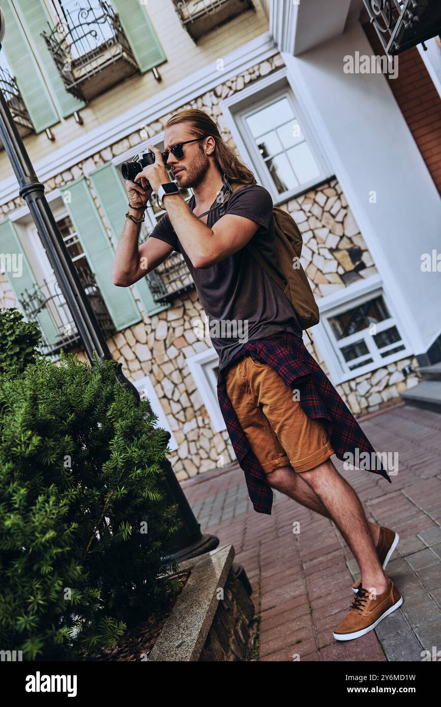 Cattura l'attimo. Un bel giovane uomo in abbigliamento casual che fotografa qualcosa mentre si trova all'aperto Foto Stock