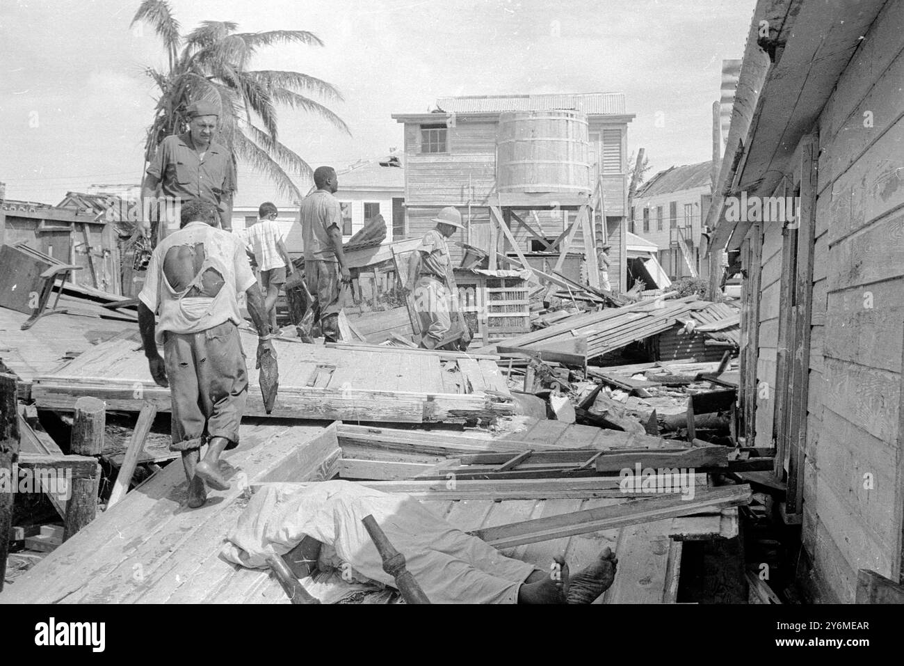 Belize, Honduras britannico: Mentre i soccorritori cercano le rovine frantumate del Belize, capitale dell'Honduras britannico, i piedi di un ragazzo ucciso quando l'uragano Hattie colpì la città, il 31 ottobre. sporgere da sotto la copertura della tela cerata della vittima. Più di 100 persone sono state uccise e migliaia di senzatetto che l'uomo visto a sinistra ha praticamente strappato la sua maglietta alle spalle 3 novembre 1961 Foto Stock