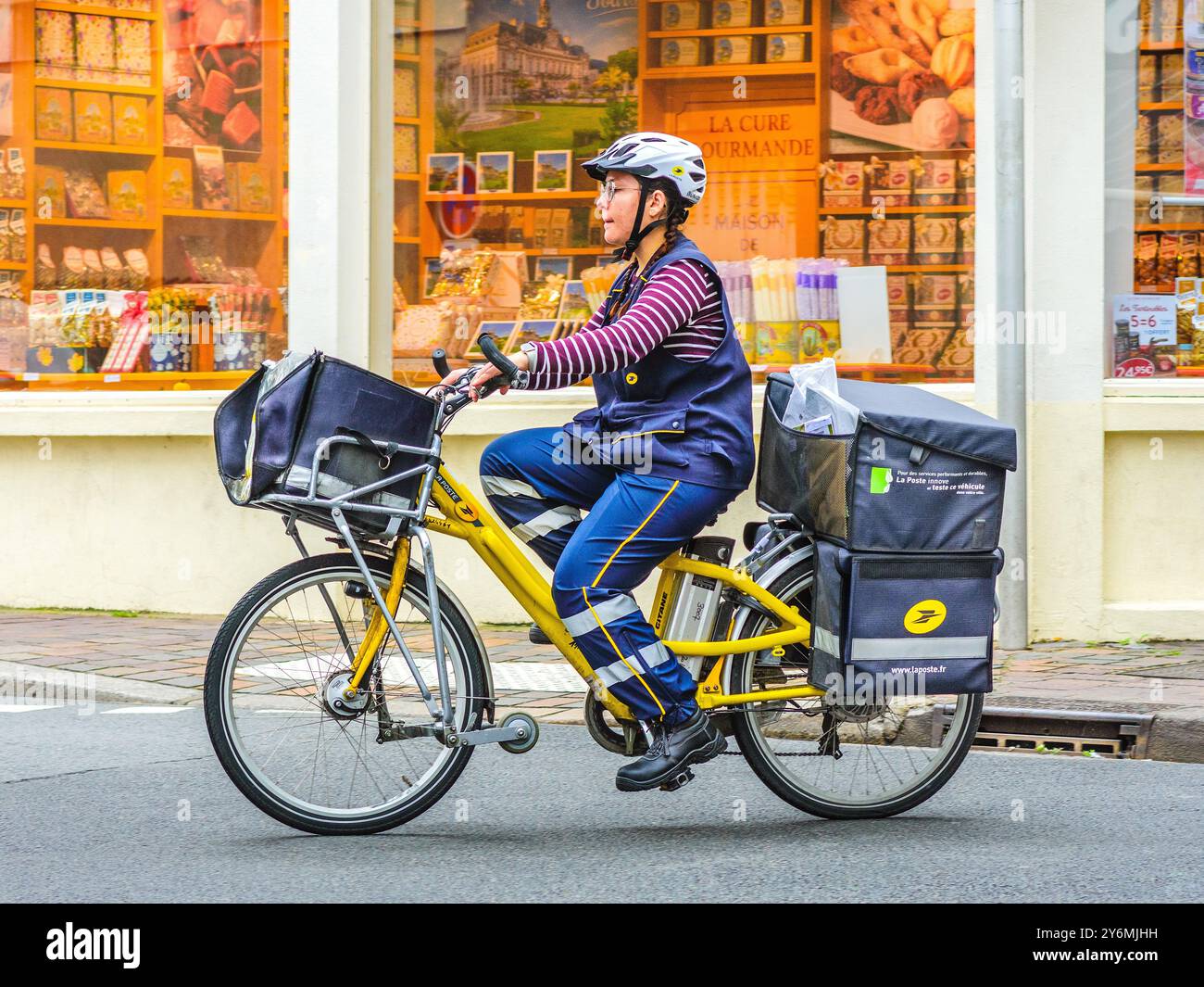 Giovane donna francese in bicicletta che consegna posta per la Poste / ufficio postale nel centro della città - Tours, Indre-et-Loire (37), Francia. Foto Stock