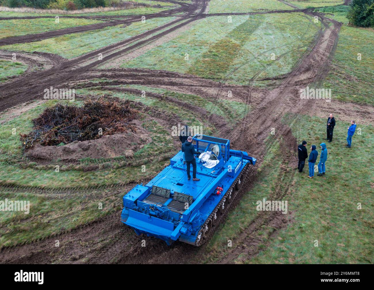 26 settembre 2024, Meclemburgo-Pomerania occidentale, Schwerin: Un veicolo blindato T55 di produzione russa è utilizzato da un'azienda privata per le operazioni di incendi boschivi e disastri per preparare un'area di compensazione della natura alla periferia della città per l'insediamento di rettili. (Vista aerea con un drone) al fine di garantire una migliore protezione delle specie, il prato deve essere dotato di una nuova struttura del suolo con l'uso di attrezzature pesanti. La città deve regolarmente trasferire lucertole di sabbia, rospi di tonnetto e altre specie protette quando le aree precedentemente inutilizzate sono preparate per la struttura Foto Stock
