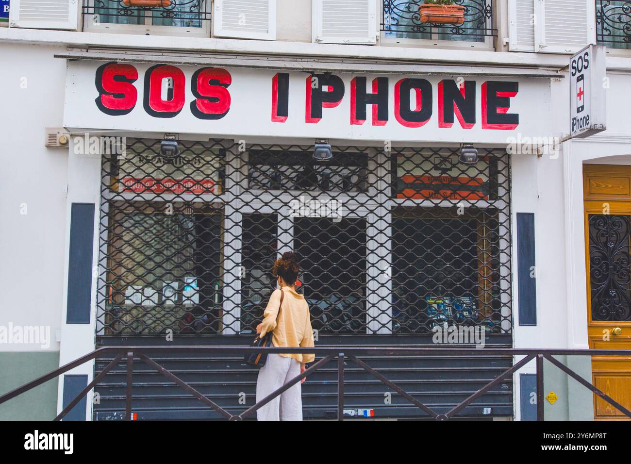 Giovane donna di fronte a un negozio chiuso di riparazione di telefoni Foto Stock