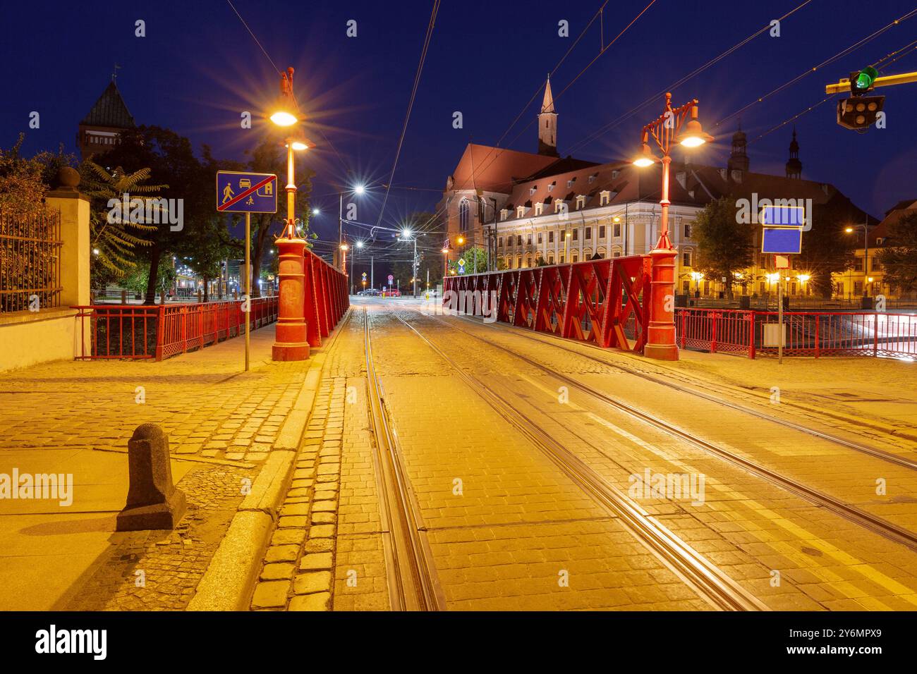 Vista notturna del Ponte Rosso di Breslavia, Polonia, illuminato da lampioni, con binari del tram ed edifici storici sullo sfondo Foto Stock